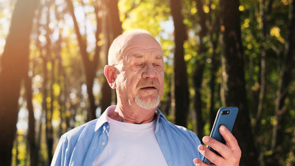 Close up portrait of senior man with a beard smiling while standing outside in sunlight.