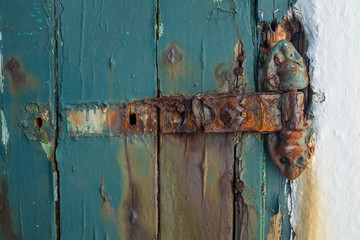 A broken rusting door hinge on a painted wooden door, paint peeling off the wood, nobody in the image