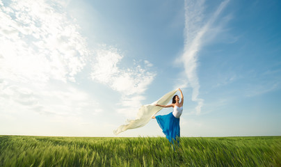 Flying dancer in the air. Happy woman ballerina in blue skirt making a big jump on Green field with...