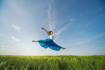 Flying dancer in the air. Happy woman ballerina in blue fabric skirt making a big jump on Green field. Summer or Spring concept