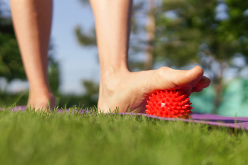 Woman massage feet with spiny plastic red massage ball in summer park. Self myofascial release concept, love your feet