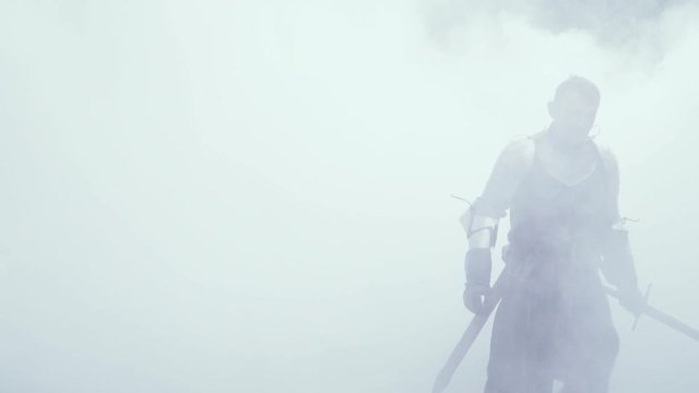 Warrior in armor with a sword in his hand is walking out of the smoke