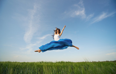 Flying dancer in the air. Happy woman ballerina in blue fabric skirt making a big jump on Green field. Summer or Spring concept
