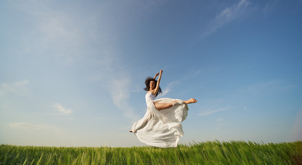 Flying dancer in the air. Happy woman ballerina in white fabric skirt making a big jump on Green field. Summer or Spring concept