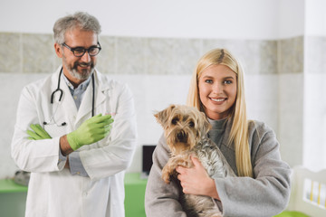 woman holding her dog at veterinary clinic. veterinarian in blurred background