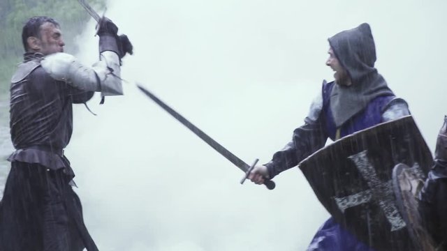 Medieval battle, men in metal armor having a sword fight smoke on the background