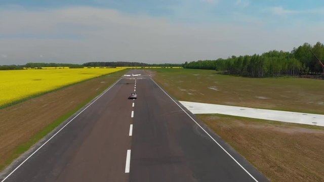 flying over propeller plane aircraft and sport car compete at speeds at the airfield. the plane is taking off aerial drone