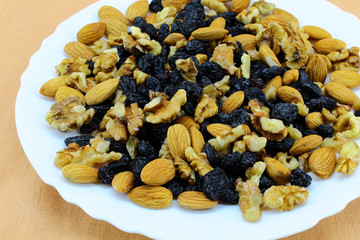In a white plate in a chaotic manner are raw useful products - walnuts, almonds, and dried grapes