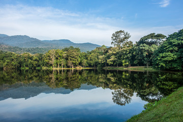 Idyllic scenic landscape of the Ang Kaew Reservoir lake, surrounded by trees and mountain in the distance.