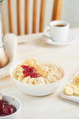 Oatmeal porridge with strawberry jam, peanut butter, banana, Chia on white wooden light background. Healthy vegan diet breakfast. Vertical.