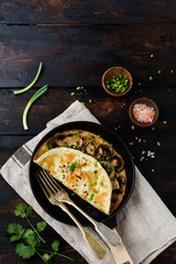 Omelette with mushrooms and green young onions on cast iron pan on old wooden background. Top view.