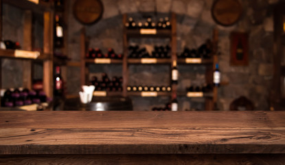 Defocused dark wine cellar background with wooden table in front - obrazy, fototapety, plakaty
