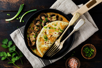 Omelette with mushrooms and green young onions on cast iron pan on old wooden background. Top view.
