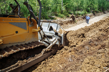 Construction of a road. Bulldozer at work. Destruction a forest. Broken and fallen trees. with a blue sky on the background. 