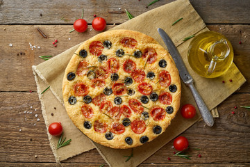 Focaccia, pizza, italian flat bread with tomatoes, olives and rosemary on wooden rustic table