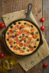 Focaccia, pizza in skillet, italian flat bread with tomatoes, olives and rosemary. Vertical, wooden...