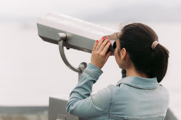 female tourist looking through coin operated binoculars with sea view