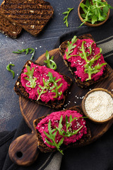 Bruschetta with beetroot hummus, arugula and sesame seeds on dark concrete background. Top view.