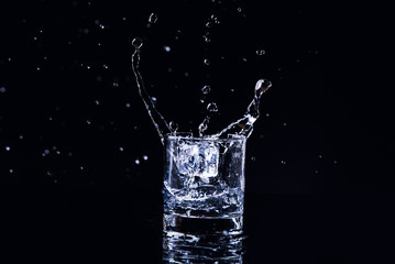 Isolated cold water in a glass with splash and cubes of ice on black background, brandy in a glass