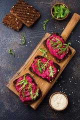 Bruschetta with beetroot hummus, arugula and sesame seeds on dark concrete background. Top view.