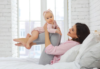 Mom and 8-month-old baby hugging on the bed in pink clothes