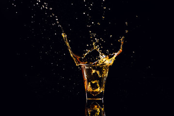 Isolated shot of whiskey with splash on black background, brandy in a glass