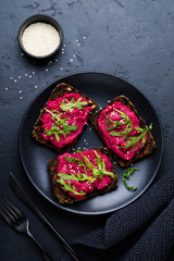 Bruschetta with beetroot hummus, arugula and sesame seeds on dark concrete background. Top view.