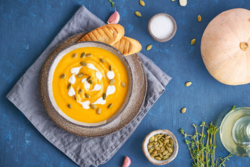 Pupmkin cream soup puree on dark blue wooden table, dietary vegetarian lunch, top view, close up.