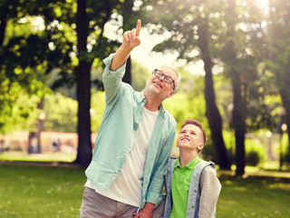 family, generation, communication and people concept - happy grandfather and grandson walking and pointing fingers up at summer park