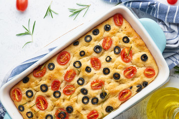 Focaccia with tomatoes, olives and rosemary in casserole, top view. Traditional Italian flat bread