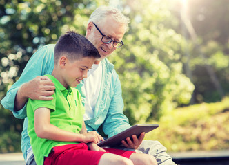 family, generation, technology, communication and people concept - happy grandfather and grandson with tablet pc computer outdoors