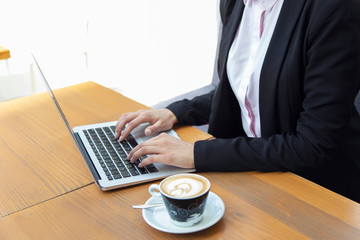 Close up of business woman hands working on laptop and having a coffee