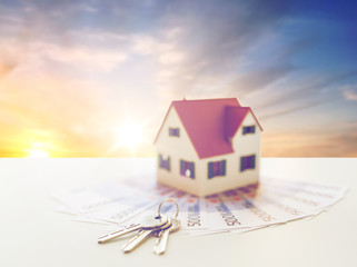 mortgage, real estate and property concept - close up of home model, money and house keys over sunset sky background