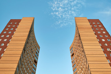 Two multi-apartment high-rise buildings stand opposite each other against a blue sky with clouds....