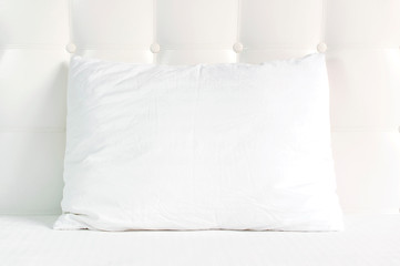 Soft white quilted pillow in bed on the background of white leather quilted headboard. Clean pillow, part of bed close-up, comfort. Quilted headboard background, bedding mockup design template