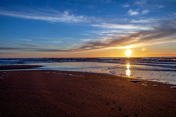 Sand beach with endless horizon and foamy waves under the bright sundown with yellow colors and clouds above the sea