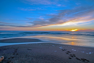 Sand beach with endless horizon and foamy waves under the bright sundown with yellow colors and clouds above the sea