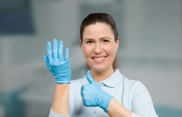 female doctor or nurse puts on her medical gloves and shows thumb up