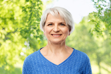 old people concept - portrait of smiling senior woman in blue sweater over green natural background