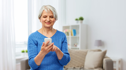 technology and old people concept - smiling senior woman using smartphone over home background