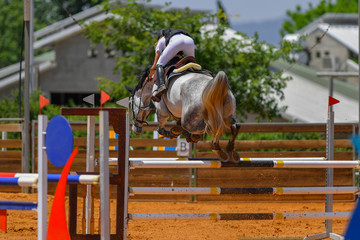 Young rider jumping over the obstacles during the horse jumping competition