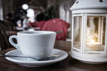 A cup of hot coffee near a lantern with a candle over cafe interior