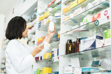 Pharmacist Asian female filling prescription medication  in pharmacy for customer or patient. small...