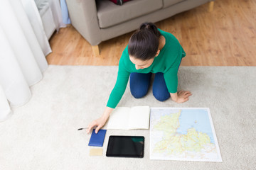 tourism, travel and vacation concept - young woman with notebook, tablet computer, passport and map going on trip