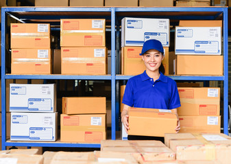 Portrait of woman delivery staff in blue uniform holding parcel box in warehouse