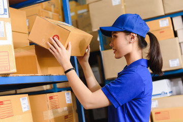 Portrait of woman delivery staff in blue uniform pick up parcel box size D in warehouse