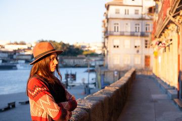 Fototapeta na wymiar Young woman with long hair walking on city street at sunrise, wearing hat and coat, enjoying happy pleasant moment of her vacations