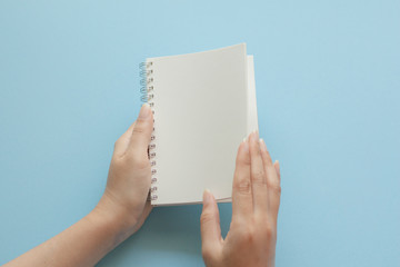 Obraz premium Young woman hand holding blank page notebook on blue background.