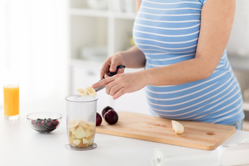 Obraz na płótnie Canvas cooking, pregnancy and healthy eating concept - pregnant woman with kitchen knife chopping fruits at home