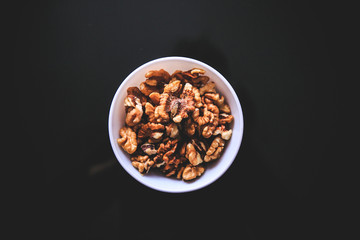 Walnuts in the white bowl on the black background taken from the top.